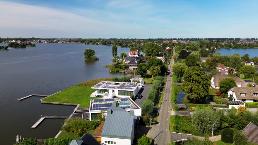Aerial view of a lakeside residential area with modern and traditional homes, tree-lined roads, and private docks. Calm water and small islands enhance the serene, nature-integrated setting.