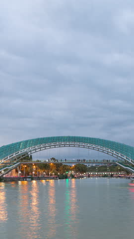 Bridge of Peace day to night transition timelapse, a bow-shaped pedestrian bridge of steel and glass over the Kura River, connecting Rike Park with Old Town in Tbilisi, Georgia