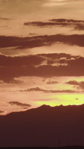 A golden sunset paints the sky in warm orange tones as dark clouds drift slowly in a high-definition time-lapse, evoking serene beauty and dramatic atmospheric contrast.