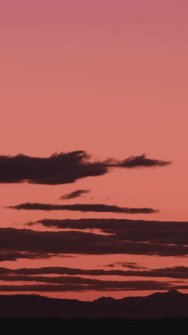 A golden sunset paints the sky in warm orange tones as dark clouds drift slowly in a high-definition time-lapse, evoking serene beauty and dramatic atmospheric contrast.