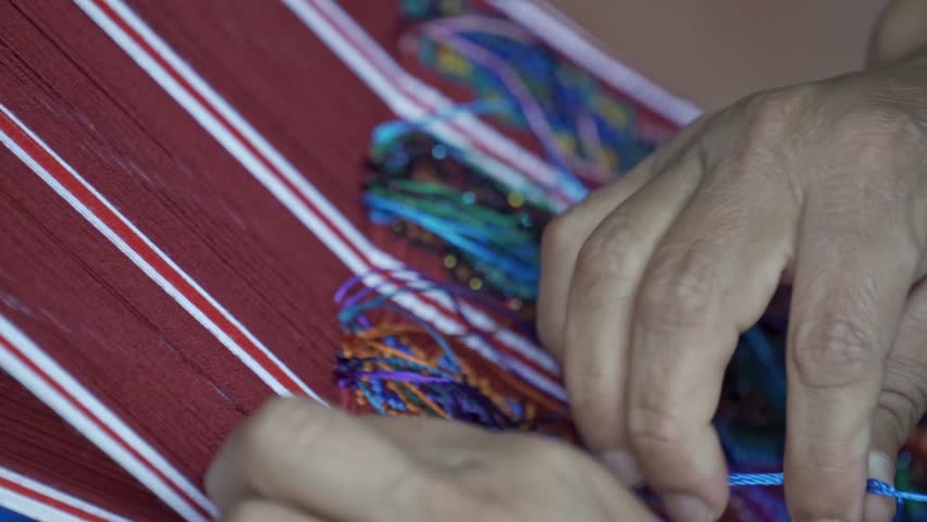 An artisan's hands meticulously weave colorful threads into a traditional textile on a loom, a craft deeply rooted in the culture of the indigenous communities surrounding Lake Atitlán, Guatemala.