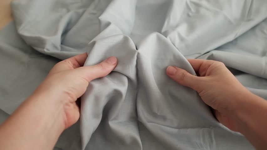Closeup video of hands touching soft blue silk fabric. Appreciating pleasant texture of high quality textile for clothes. Soft and cozy textile. Premium quality silk fabric for luxury clothes.