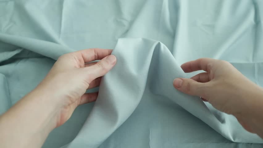 Closeup video of hands touching soft blue silk fabric. Appreciating pleasant texture of high quality textile for clothes. Soft and cozy textile. Premium quality silk fabric for luxury clothes.
