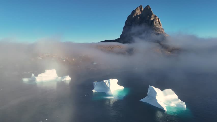Town Uummannaq during summer in northern West Greenland beyond the Arctic Circle. Greenland, Danish territory. Large mountains and glaciers in the background. Misty morning. Fjord in Greenland. Aerial