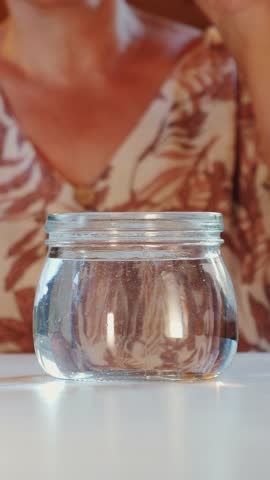 False teeth are immersed in dentures in glass of water. Elderly person putting dentures in glass of water. Vertical video