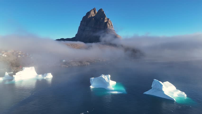 Town Uummannaq during summer in northern West Greenland beyond the Arctic Circle. Greenland, Danish territory. Large mountains and glaciers in the background. Misty morning. Fjord in Greenland. Aerial