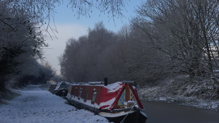Canal boat Narrow marine transport on the water in winter with smoke coming out of chimney with snow and frozen landscape UK 4K