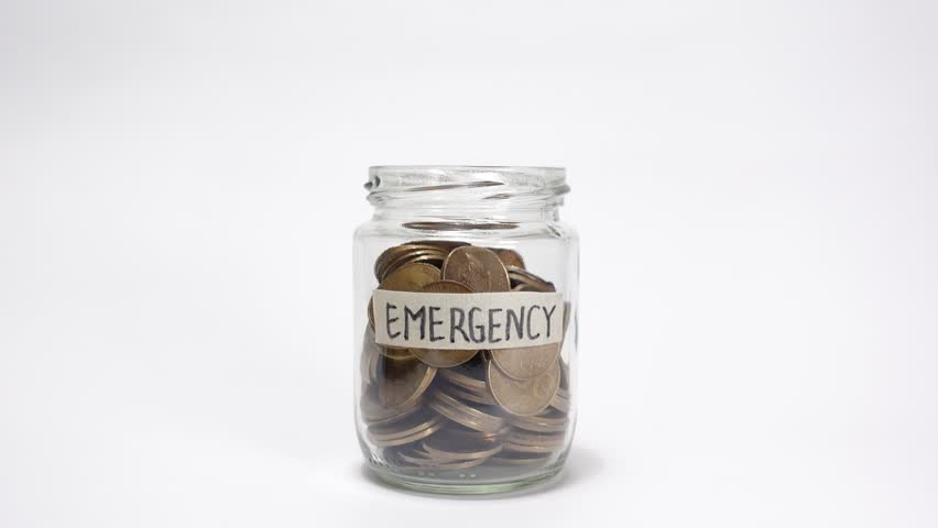 A hand putting gold coins into a jar labeled Emergency, symbolizing financial savings, preparedness, and the importance of building a safety net for unexpected situations.