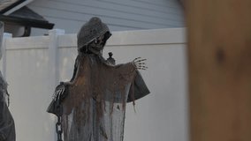 Tattered hooded skeleton prop with glowing red eyes stands in a suburban yard by a white fence. Halloween outdoor decoration with burlap cloak, chains, and a bony hand in evening light. - Powered by Shutterstock - Get 15% off with code: PIKWIZARD15