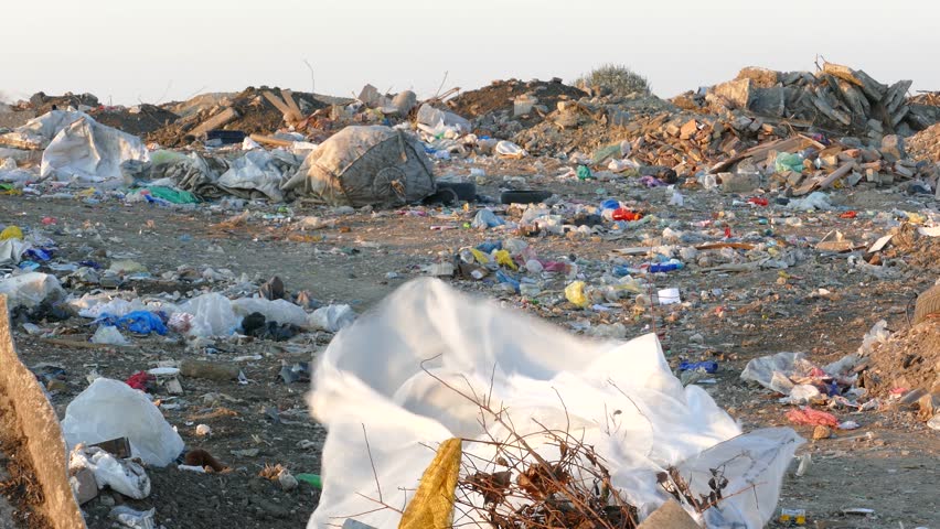 Garbage dump environmental pollution and plastic bags blowing in the wind. There are lots of plastic bags, bottles, and other waste are scattered all over the dump site. Landfill near the city