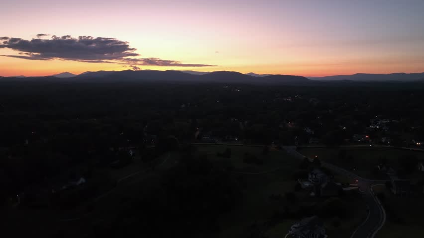 Golden sunset behind Mountains in America. Dusk scene with driving cars on rural road in suburbia. Aerial rising wide shot. Quiet and peaceful atmosphere scene on summer.