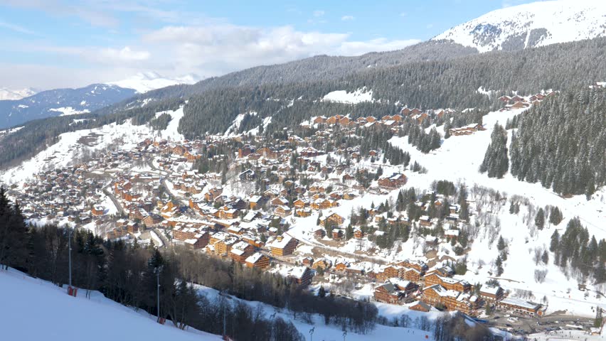 Sunlight bathing snow covered chalets and slopes of ski resort. Revealing panoramic french alps mountain landscape in winter