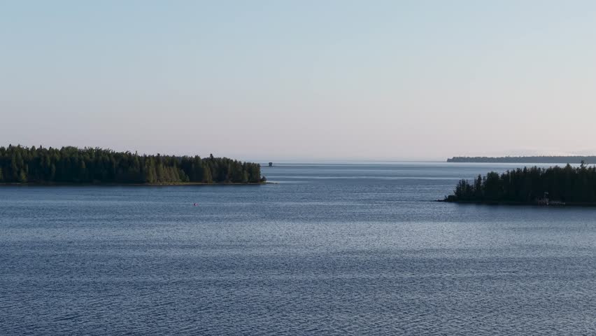 Aerial drone footage of a calm lake with tree-lined islands and distant horizon in Michigan’s Upper Peninsula wilderness.