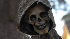 Close-up hooded skeleton skull with glowing red LED eyes and a creepy grin. Spooky Halloween decoration with tattered burlap cloak and netting in an outdoor yard. - Powered by Shutterstock - Get 15% off with code: PIKWIZARD15