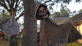 Tattered hooded skeleton with glowing red eyes stands in a suburban yard at dusk. Burlap cloak, bony hand, and a tree background create a spooky Halloween display. - Powered by Shutterstock - Get 15% off with code: PIKWIZARD15