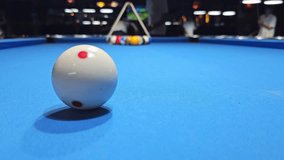 White cue ball with red spots on blue billiard table with triangle rack of colored balls in background inside pool hall - Powered by Shutterstock - Get 15% off with code: PIKWIZARD15