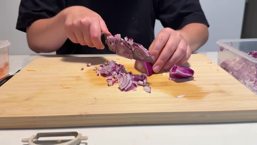 Woman skillfully chops red onion on wooden cutting board, using sharp knife for culinary dish preparation