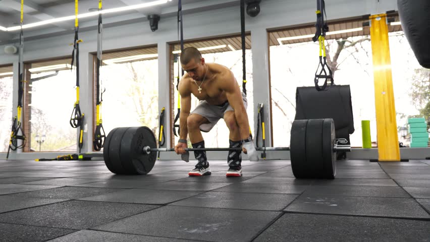 Strong athletic man performing deadlift exercise in a modern gym, showcasing strength and determination while lifting heavy weights with focused posture and dynamic movement