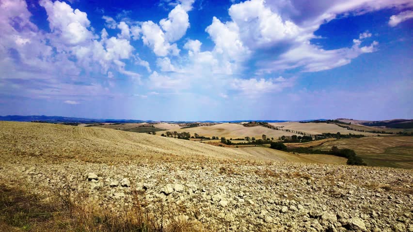 4K  aerial of the Crete Senesi near Siena Tuscany Italy rolling hills farmland and cypress ridge under blue sky and clouds serene rural landscape perfect for travel tourism nature and agriculture