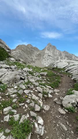 Steep mountain trail stretching ahead in a dramatic POV view, revealing rugged terrain and alpine cliffs under a bright sky in the Canadian Rockies