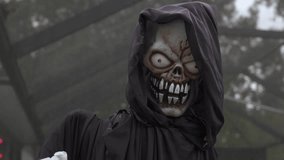 Close-up of a hooded grim reaper prop with a skull face and sharp teeth. Red glowing eyes and a black cloak create a spooky Halloween decoration outdoors. - Powered by Shutterstock - Get 15% off with code: PIKWIZARD15