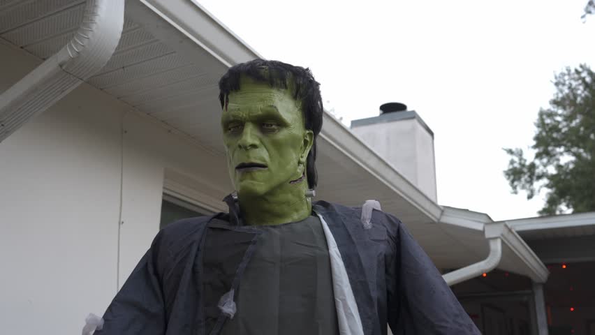 Close-up of a green monster prop with outstretched hands and a ragged coat. Spooky Halloween decoration outside a house creating a scary horror mood.