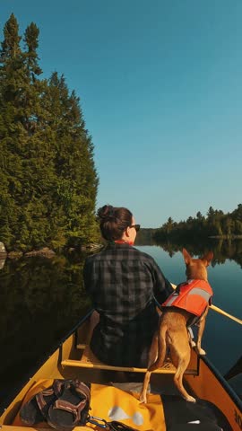 A vertical shot of a woman and her dog canoeing on a calm lake in Algonquin Park under clear skies
