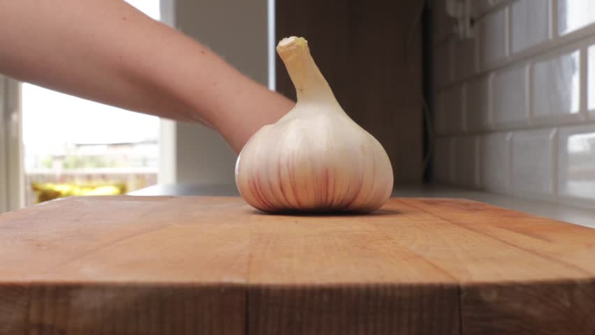 Peeling garlic on wooden cutting board. Close-up of hands using knife to clean fresh garlic for cooking preparation.