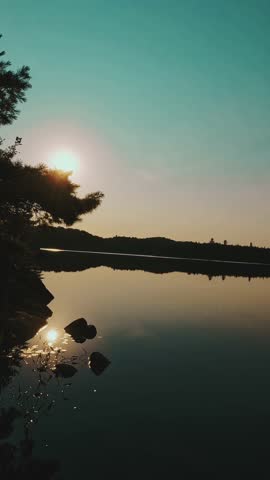 A cinematic shot of Algonquin Park dawn, where calm waters mirror trees and the rising sun
