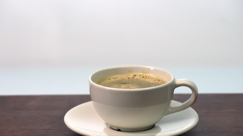 Adding whole 3 organic sugar cube in hot ceramic coffee cup on white saucer, on wooden table morning beverage, hot aromatic coffee, minimal style, inviting and cozy breakfast refreshment.