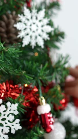 Vertical Asian woman decorating christmas tree with tinsel garland in living room house. Merry christmas and happy new year concept. Girl putting Xmas ornaments on spruce branches. Family cozy moments