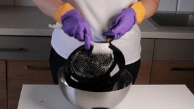 woman cleaning greasy frying pan with dish brush wearing protective rubber gloves, scrubbing bottom of black pan in kitchen over large bowl, concept of household chores, sanitation, cleaning service - Powered by Shutterstock - Get 15% off with code: PIKWIZARD15