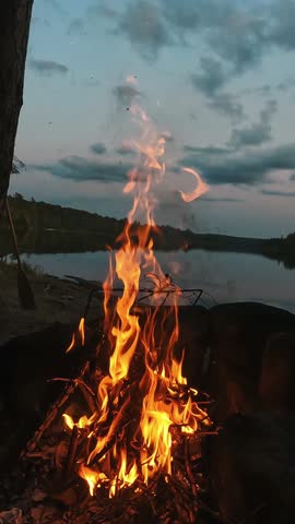 A cinematic Algonquin campfire at sunset, where glowing flames meet the calm wilderness horizon