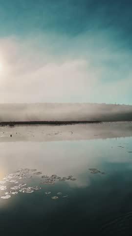 A still lake perfectly mirrors the misty, forested shoreline and the blue sky above in Ontario, Algonquin Park, Canada