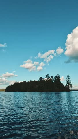 A wooded island surrounded by a pristine backcountry lake and clear sky with white clouds in Algonquin Park, Ontario, Canada
