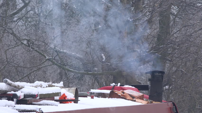 Canal boat Narrow marine transport on the water in winter with smoke coming out of chimney with snow and frozen landscape UK 4K