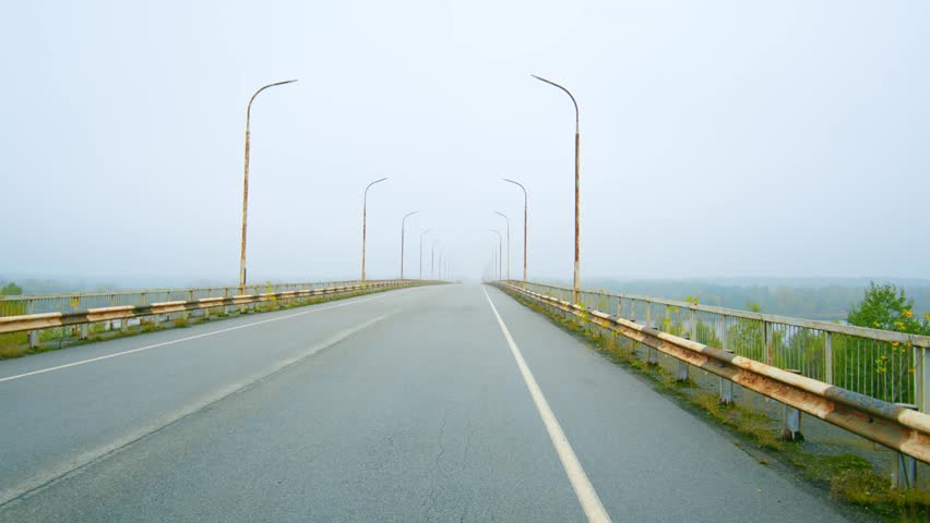 Footage captures the eerie and atmospheric scene of the abandoned Paryshivskyi Bridge spanning the Pripyat River within the Chernobyl Exclusion Zone. The bridge, shrouded in mist or fog, features rust