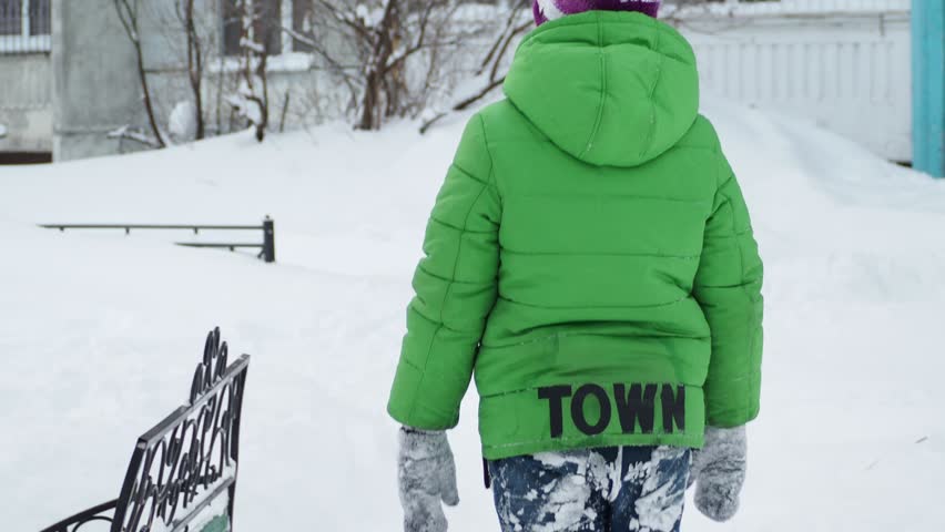 boy walks down an icy street on a snowy day. Teenage boy in winter clothes walking during snowfall. Winter activities for children in the fresh air. Child in a warm hat walking in the street in winter