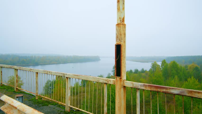A serene yet poignant view of the Pripyat River as seen from the Paryshivskyi Bridge, shrouded in a misty morning fog. The surrounding autumnal forest and the calm waters reflect the quiet, untouched