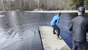 Blue jacket man and a black clothed man with a cap on a wooden pier pulling in synchrony a rope ferry that is stuck behind and ice sheet in frozen lake. Neverthless their effort the ferry is stuck. - Powered by Shutterstock - Get 15% off with code: PIKWIZARD15