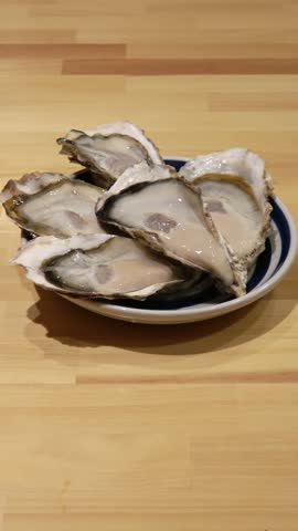 Vertical shot: Five fresh, plump oysters are arranged on a plate.