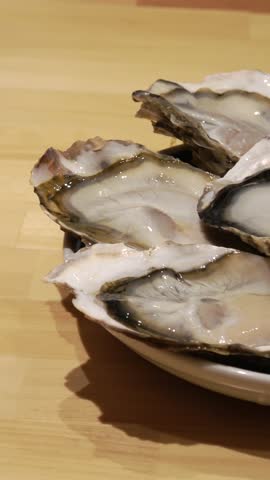 Vertical close-up: Five fresh, plump oysters on a plate.