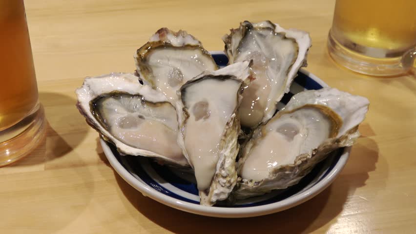 Five fresh, plump oysters are arranged on a plate.