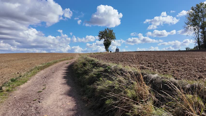 Scenic panoramic pan across a plowed farm field under a blue cloudy sky in the countryside