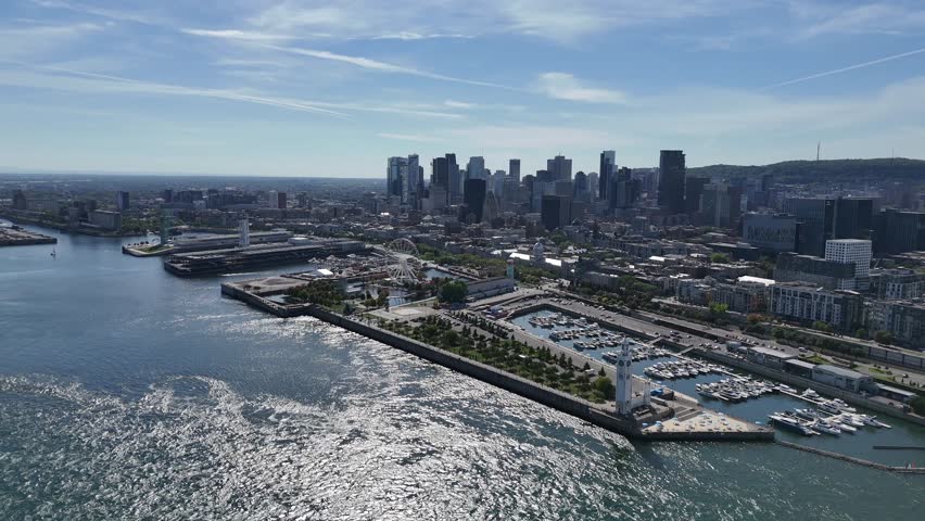 Drone flies over St. Lawrence River, showing Old Port Montreal with lights and Ferris wheel, then pans left to reveal Parc de Dieppe and boats in the marina below