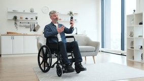 Mature Caucasian man in wheelchair using smartphone for video call in modern bright living room. Depicts inclusive technology use and connectivity. - Powered by Shutterstock - Get 15% off with code: PIKWIZARD15