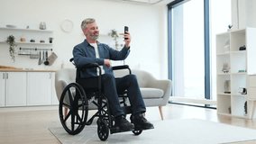 Caucasian man with gray hair sitting in wheelchair using smartphone for video call. Interior setting conveys warmth and modern design, highlighting connectivity, independence, and accessibility. - Powered by Shutterstock - Get 15% off with code: PIKWIZARD15