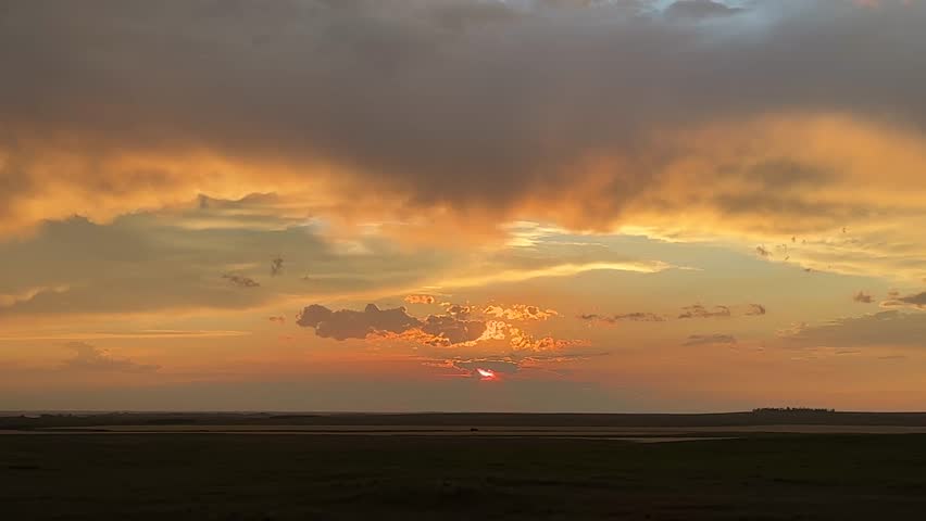 Agricultural field at sunset with glowing sky, dramatic clouds, and wide prairie view, highlighting rural life, scenic beauty, and open countryside atmosphere in Alberta, Canada.