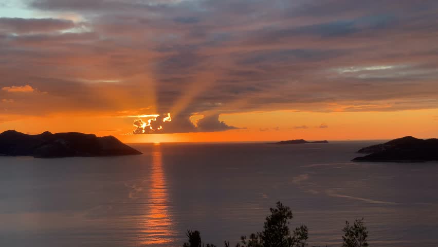 Sunset casting golden rays over calm sea and silhouetted islands with colorful sky background video