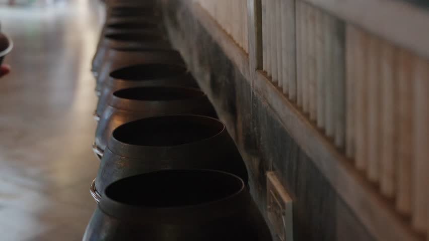 A person placing coins into a row of alms bowls inside the temple of the Reclining Buddha at Wat Pho, Bangkok, Thailand